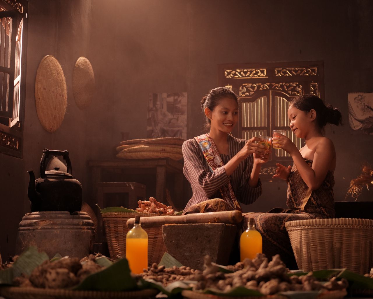 Two women in traditional attire enjoying drinks in a cozy market setting with baskets and spices.