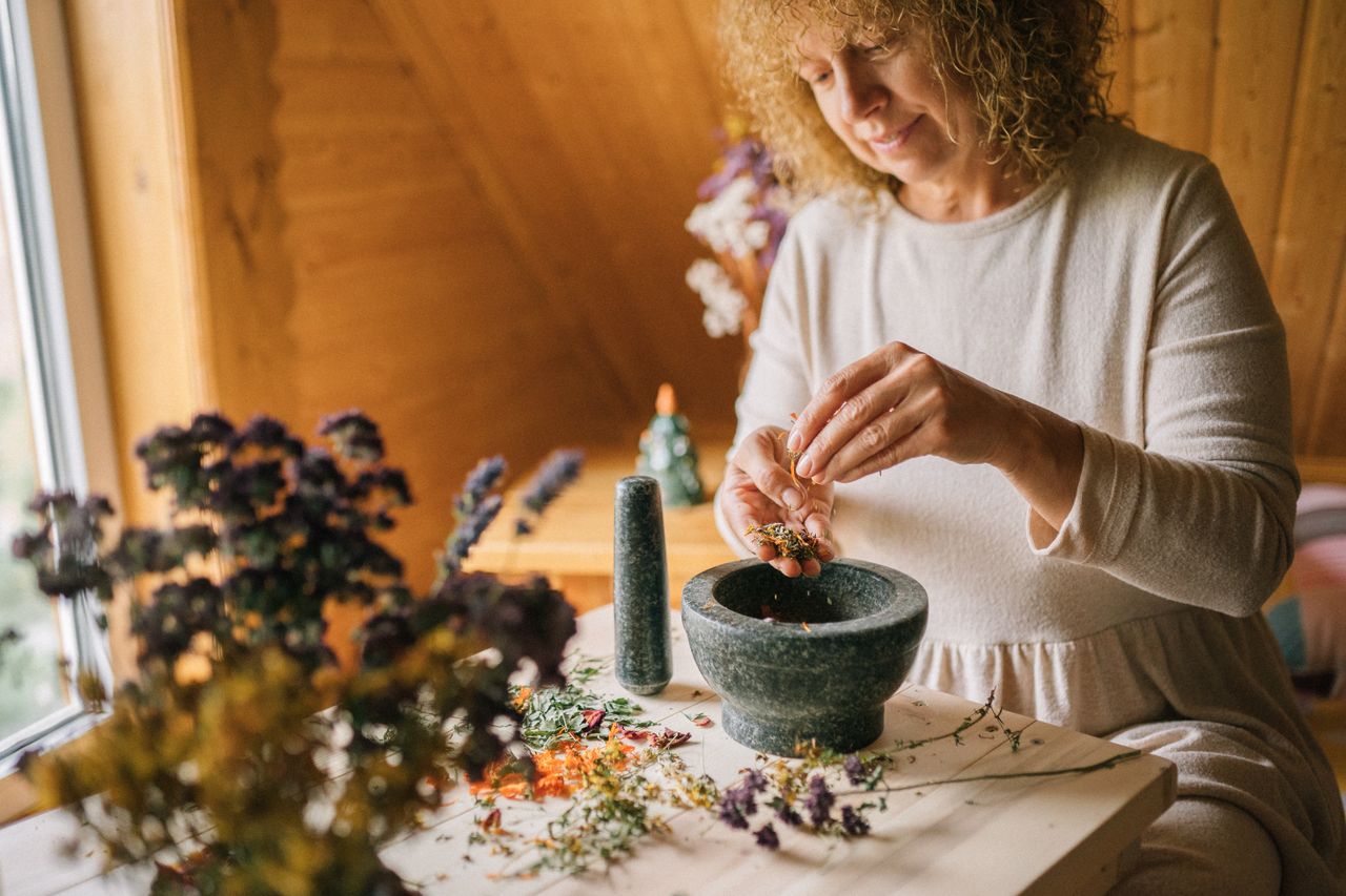 A woman preparing herbs with a mortar and pestle in a cozy wooden room.